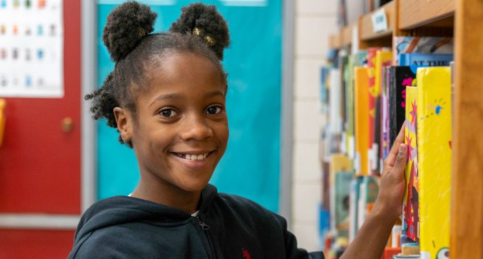 A child pulling a book from a bookshelf in a library.