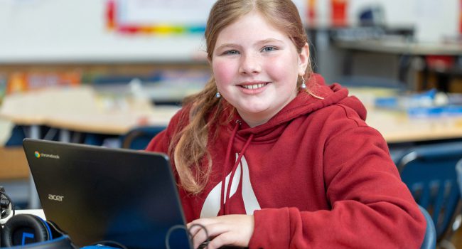 A girl smiles as she uses a computer.