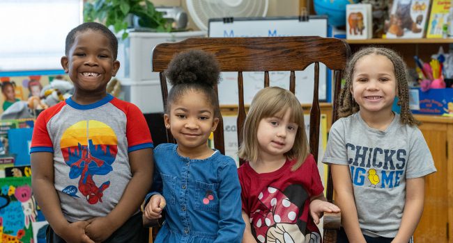 Four young children stand next to one another and smile.