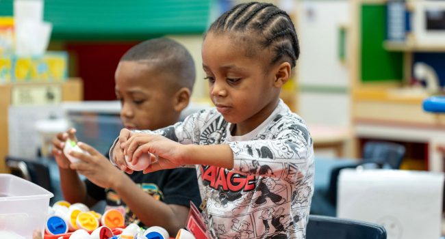 Two young children at a table putting eggs together that have letters in them.