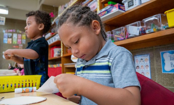 Young children in a classroom cutting and gluing projects.