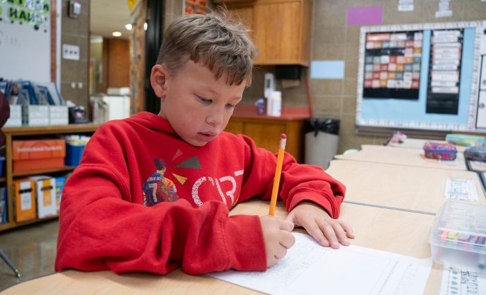 A child in a classroom writing on a piece of paper.