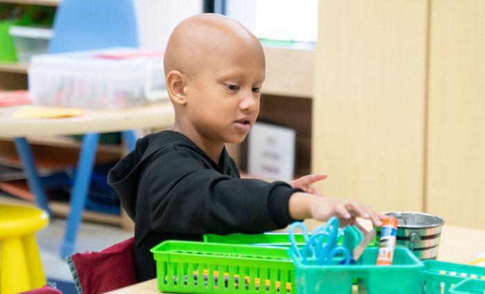 A young child at a table reaching for a glue stick.