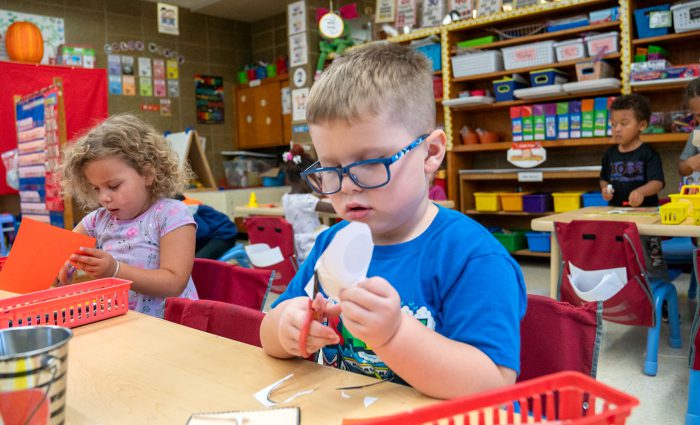 Young children in a classroom using scissors.