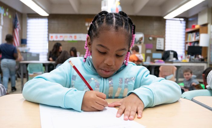 A young child in a classroom writing on paper.