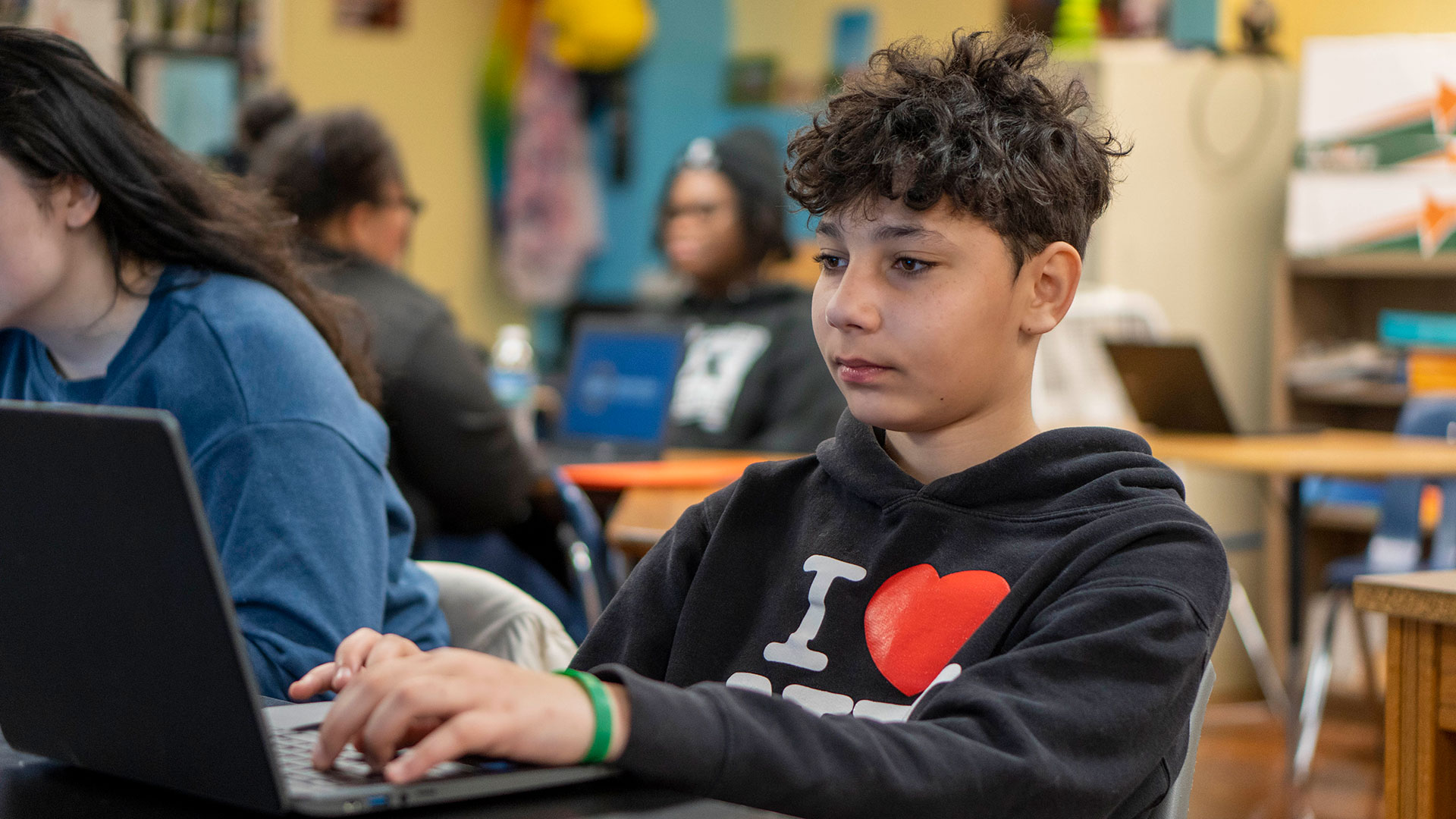 A boy types on a laptop in a classroom.