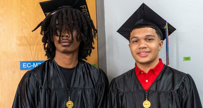Two graduates in black cap and gowns.