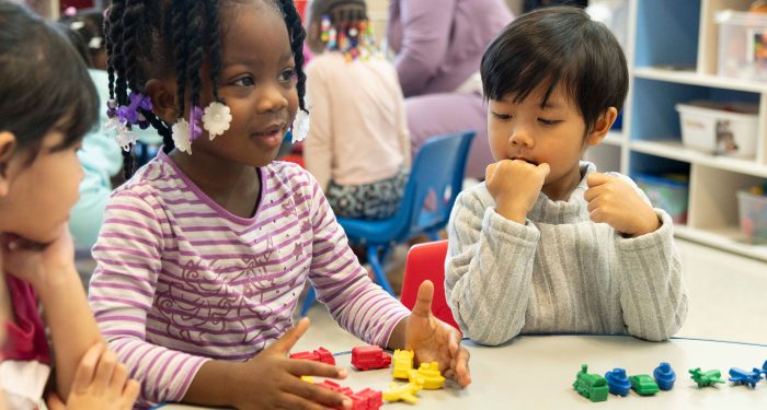 Young children at a table using small toys for counting.