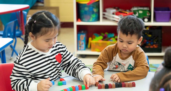 Two young children at a table play with blocks.