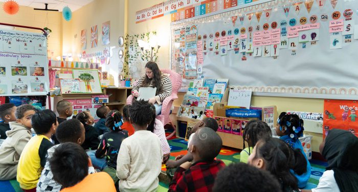 A teacher in a chair reads to her young students on the rug in front of her.