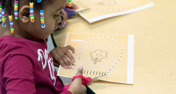 Close-up of a young child cutting out a paper mitten.