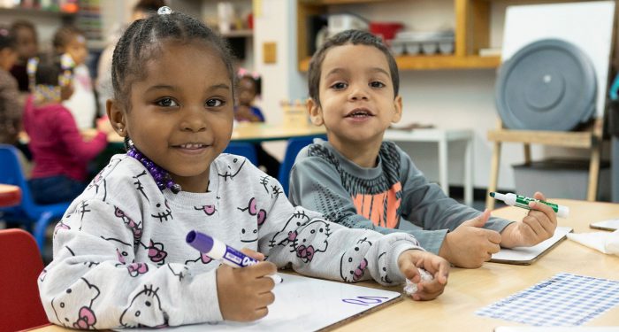 Young children at a table writing on small whiteboards.