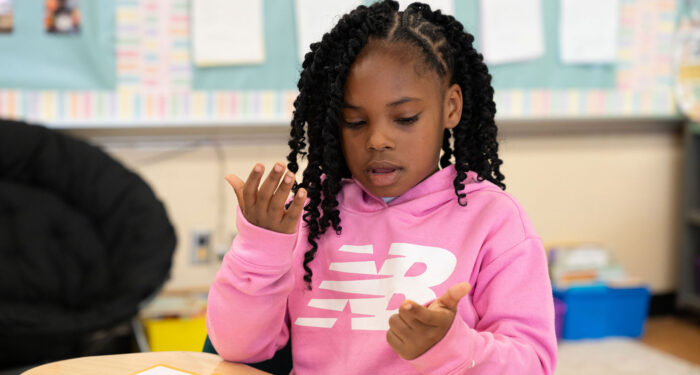 A young child in a classroom using her fingers to count.
