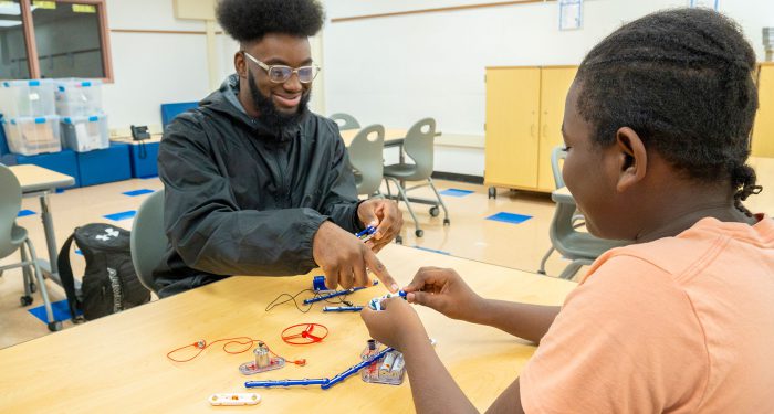 A teacher helps a student create an electrical circuit.