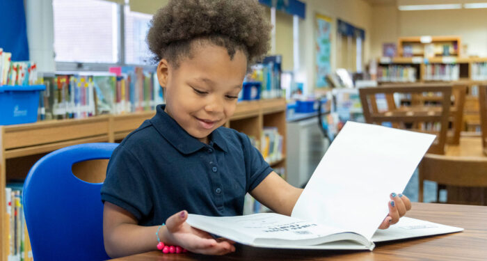 A young girl in a library looking at a picture book.