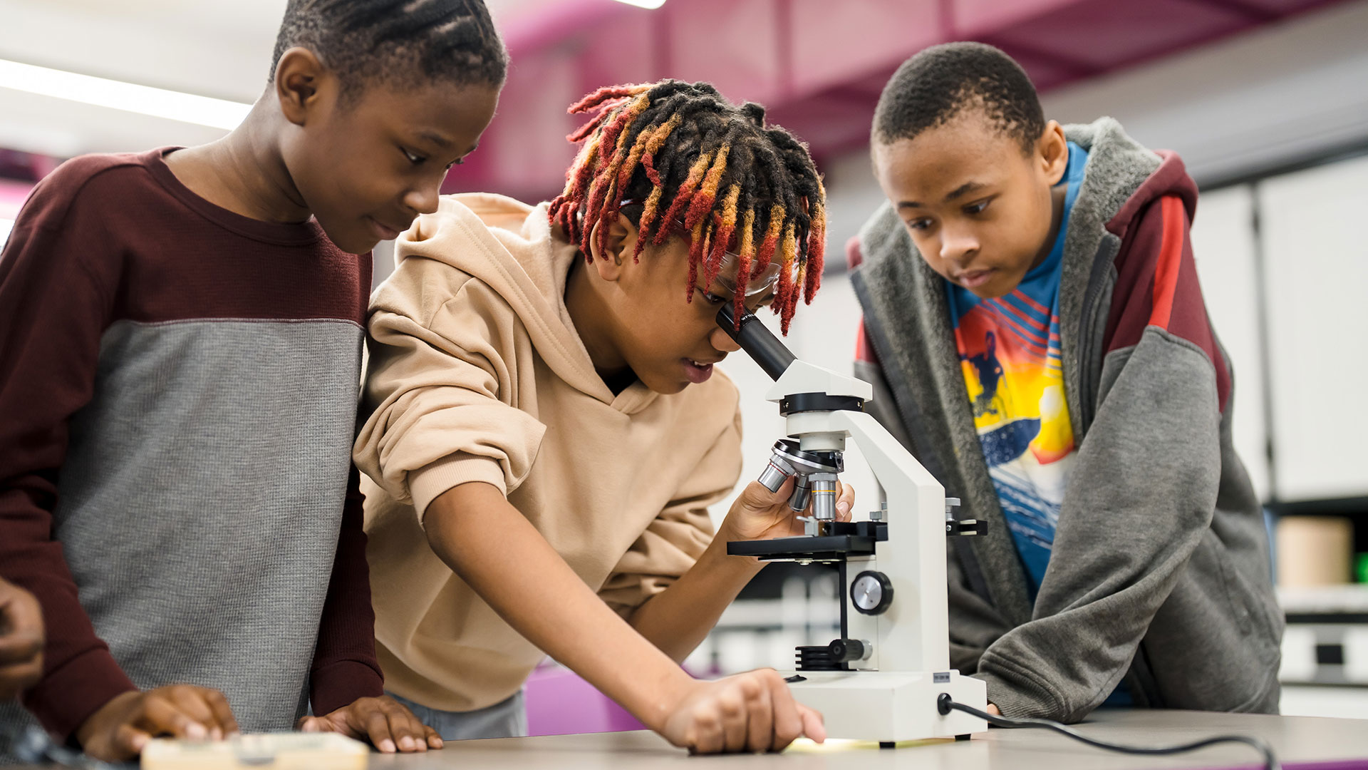 A student looks through a microscope while two other students watch.