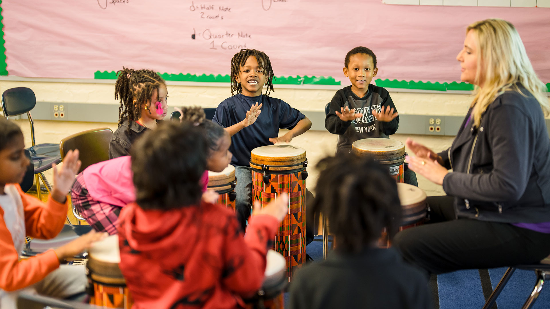 Young students play drums with their teacher.