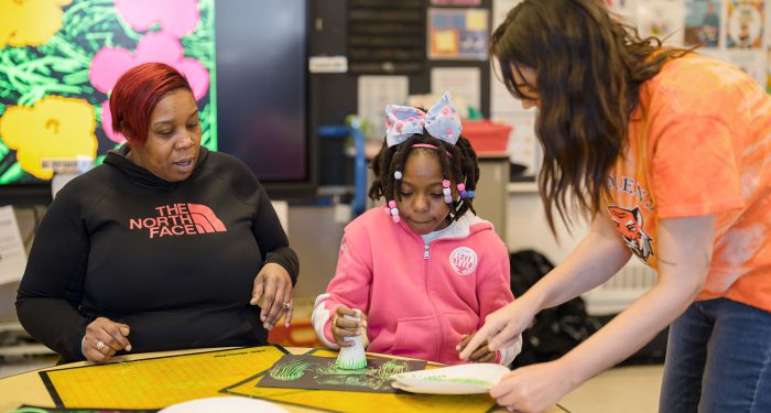 Two teachers help a student with an art project.
