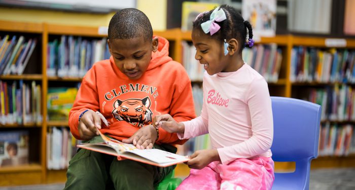 Two young students in a library looking at a book together.