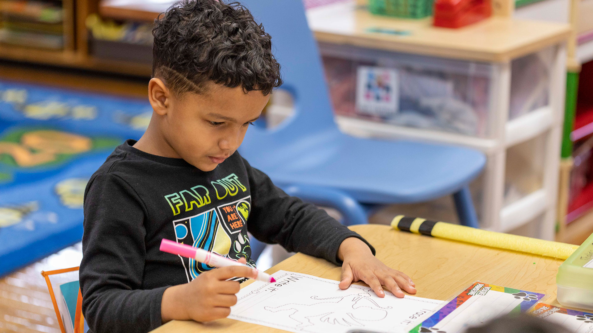 A young boy sitting at a table writing on a worksheet.
