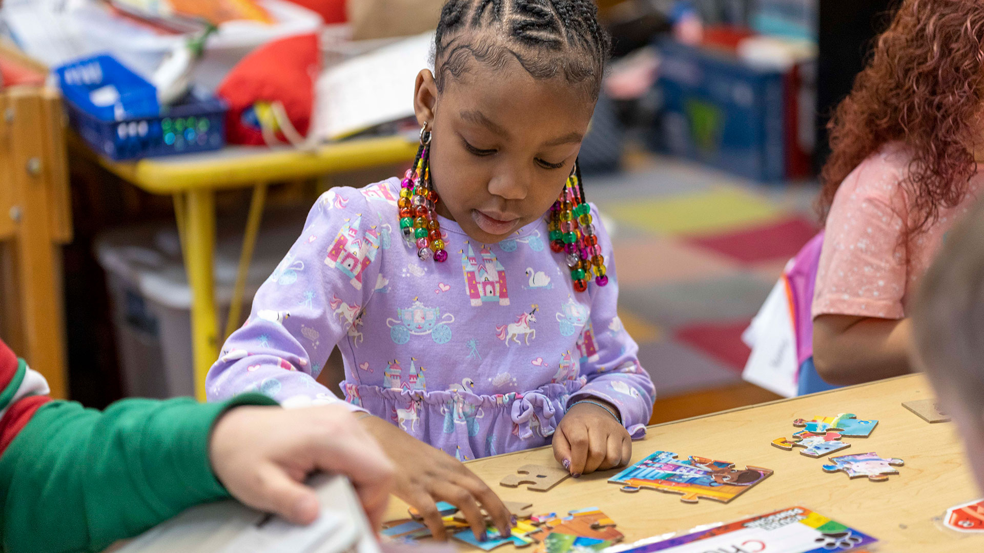 A young girl at a table puttting a wooden puzzle together.