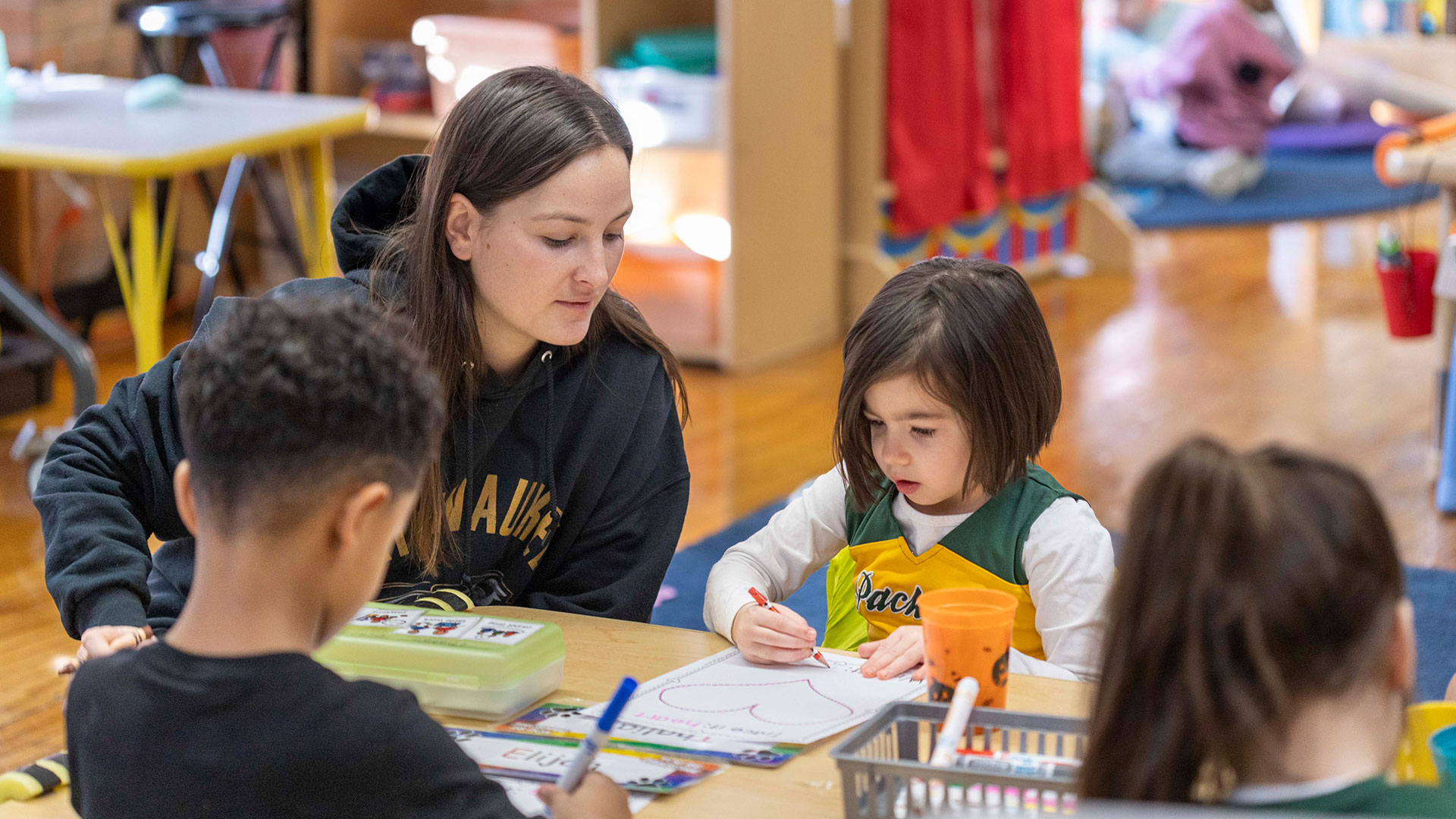 A teacher sits with her students as they draw.