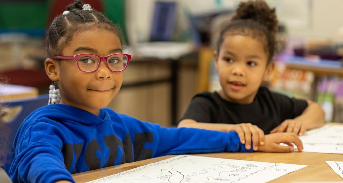Two young girls at a table smiling.