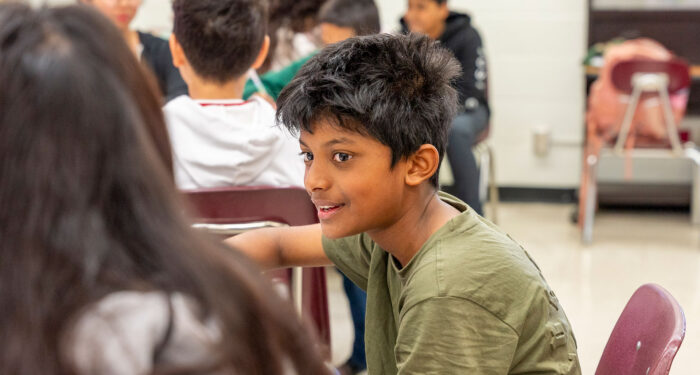 A child smiles while talking to another child in a classroom.