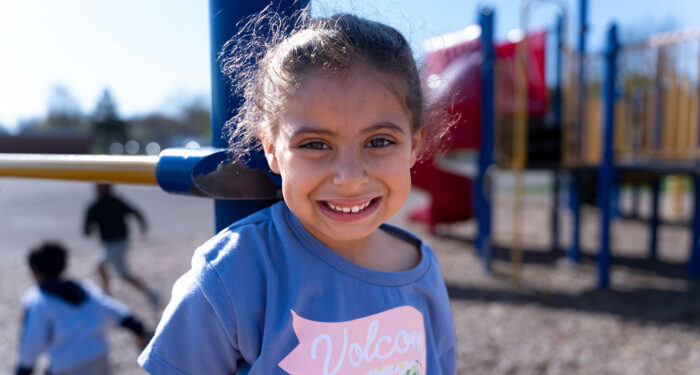 A girl on a playground smiling.