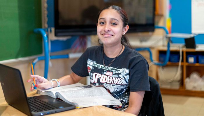 A girl with a Spiderman shirt reads from a book.