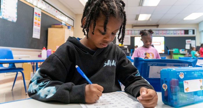 A student in a classroom writing on a worksheet.