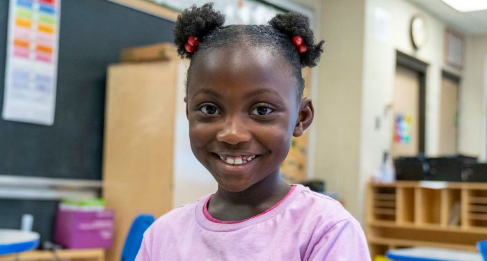 A young girl in a classroom smiling.