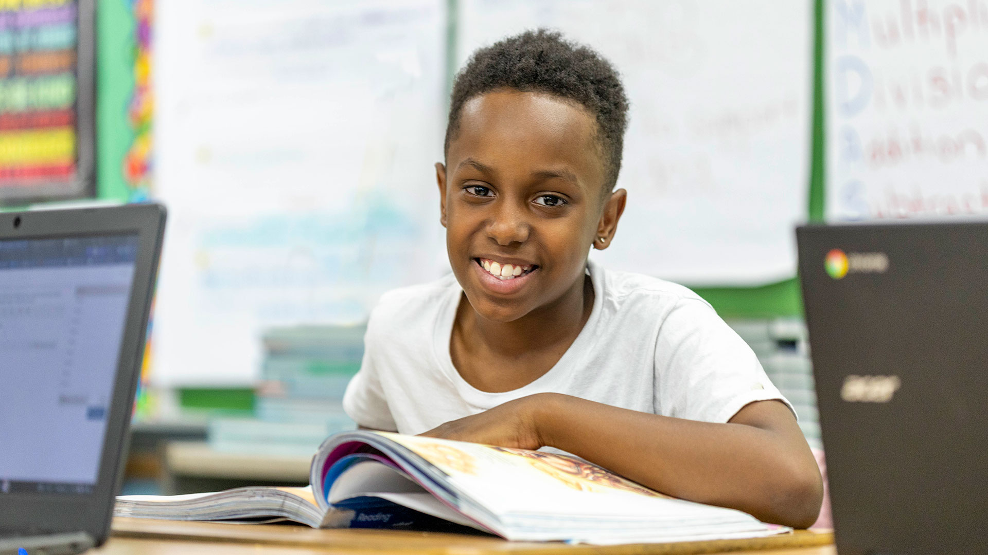 A boy smiles as he reads his workbook.