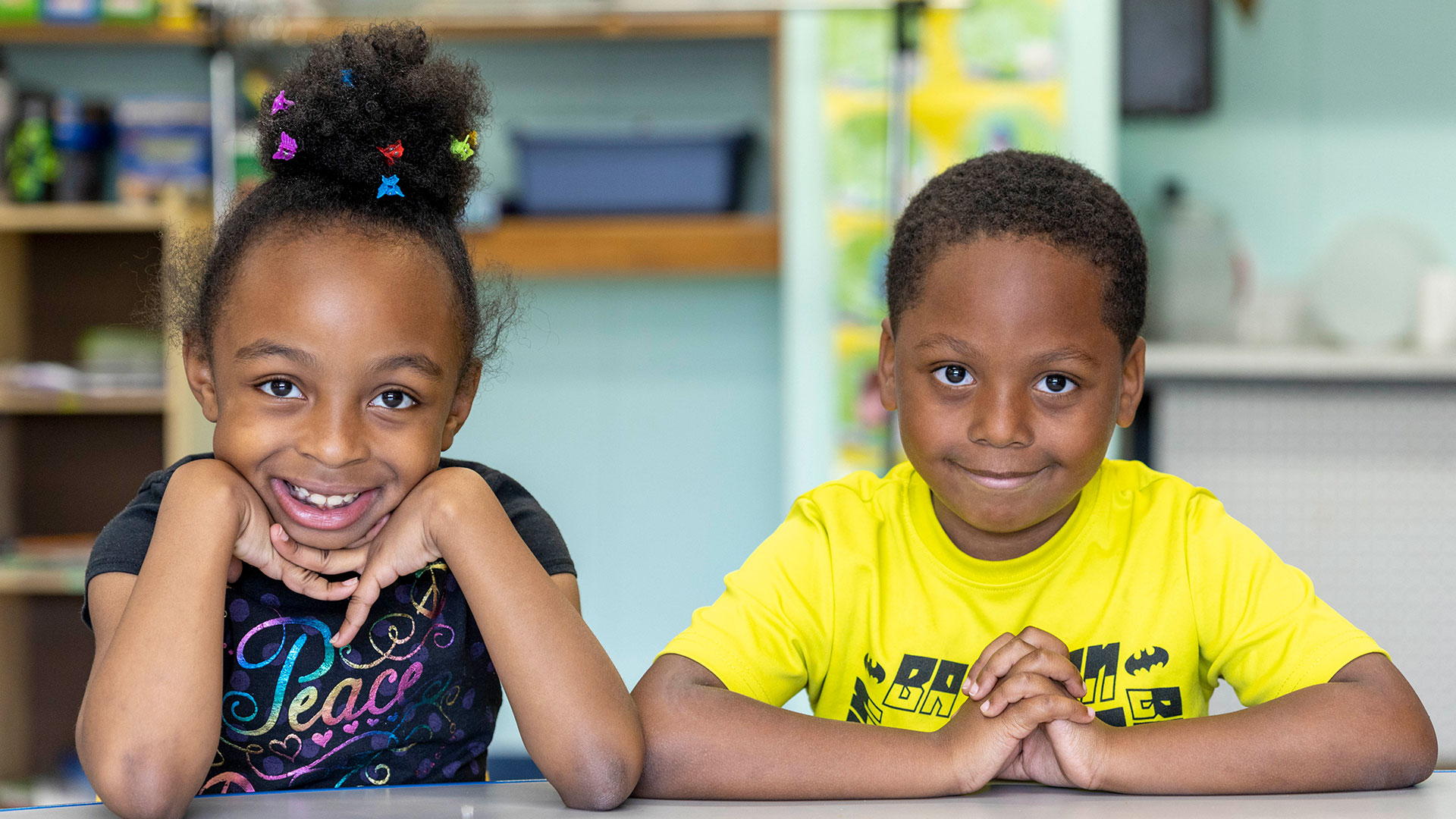 A young boy and girl sit at a table smiling.