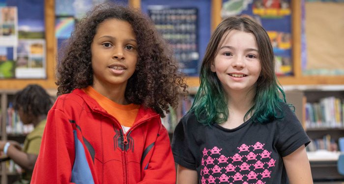 Two girls stand next to eachother and smile.