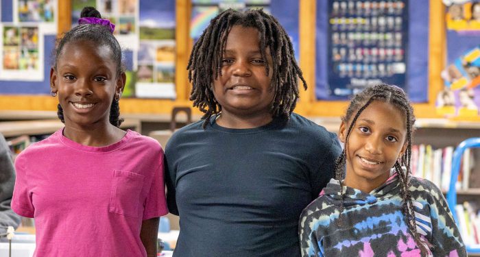 Three students smile as they stand shoulder to shoulder.