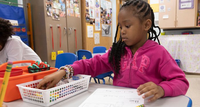 A young girl sitting at a table reaching into a bin with crayons.