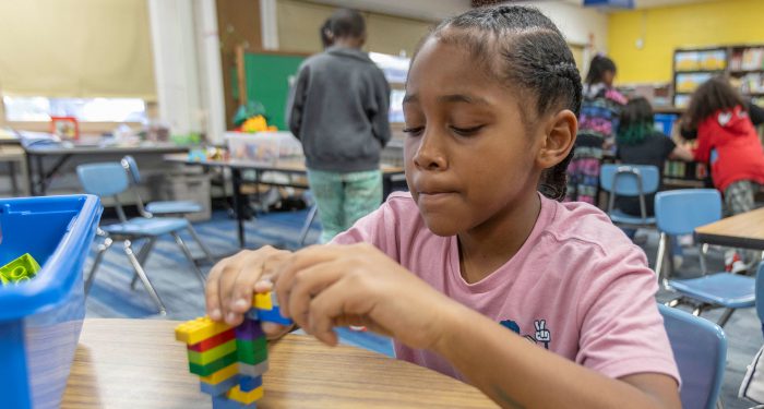 A student sitting at a table putting Lego together.
