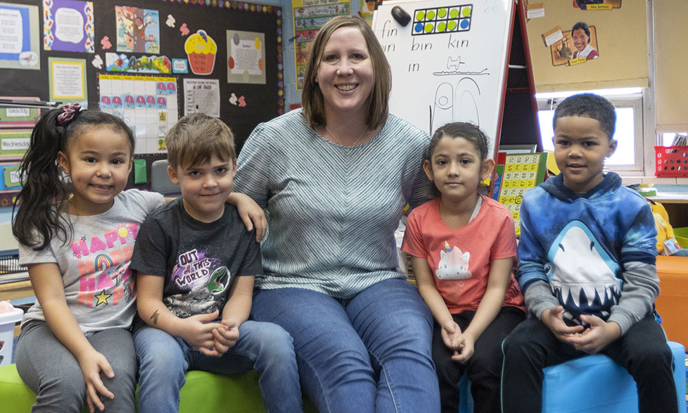 A teacher and her young students smile at the camera.