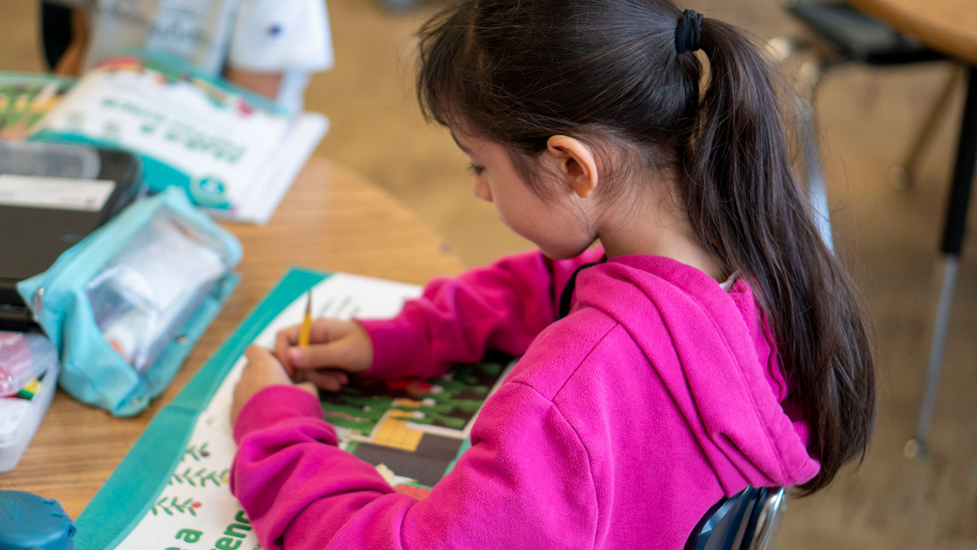 A young girl sits at a table and writes in a workbook.