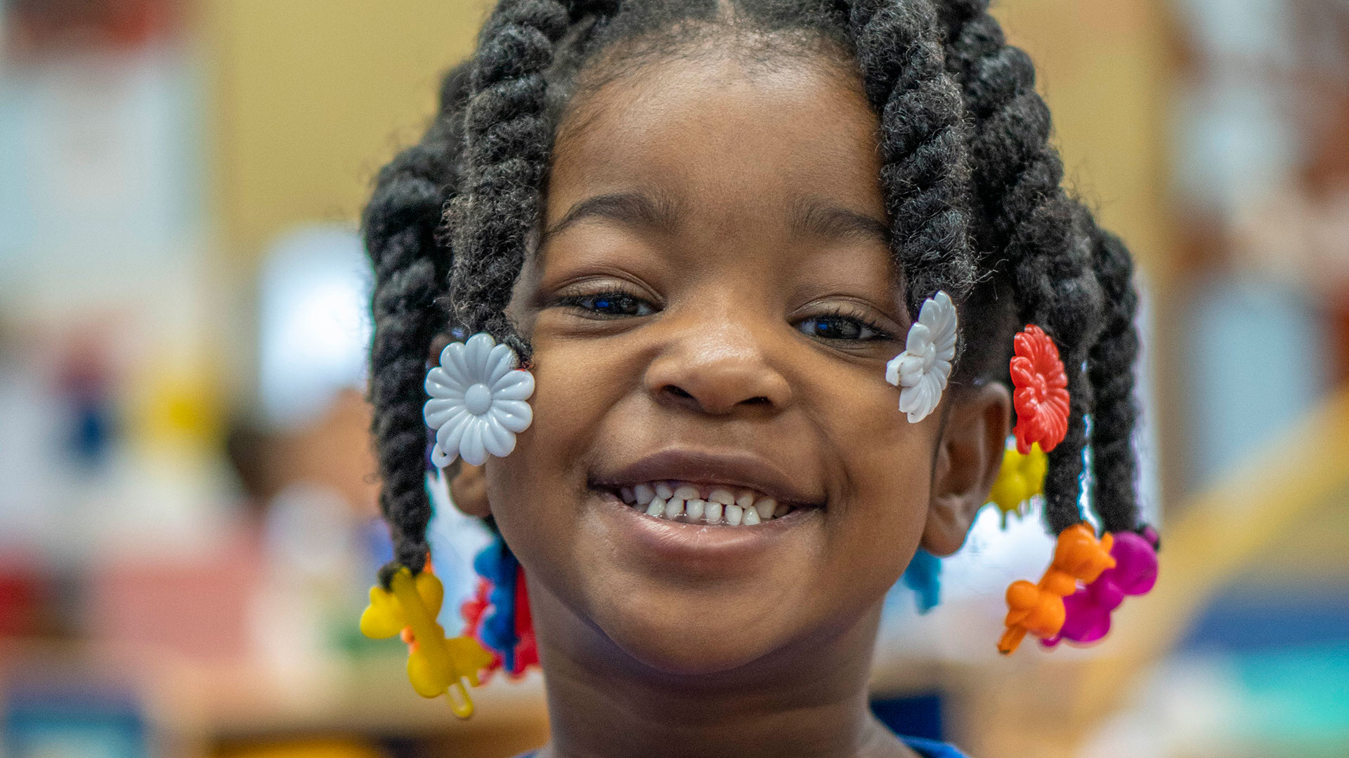 Close-up of a smiling young girl with braids and barrettes.