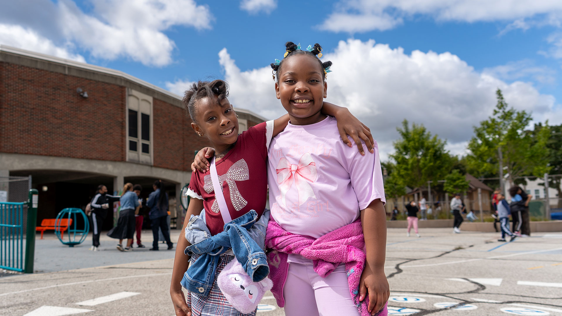 Two girls on a playground with their arms around one another.