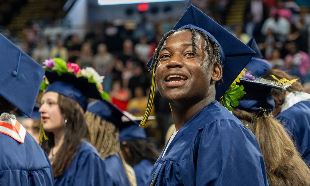 A smiling graduate looks into the crowd.