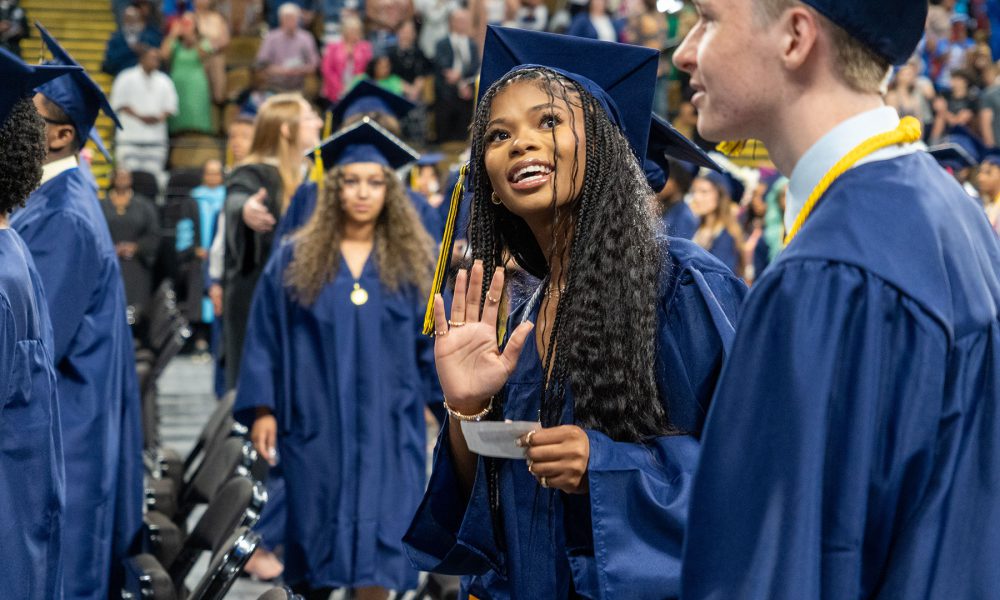 A graduate smiles and waves.