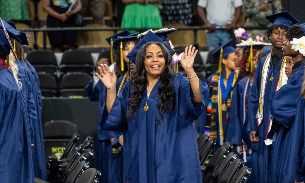 A graduate smiles and waves.