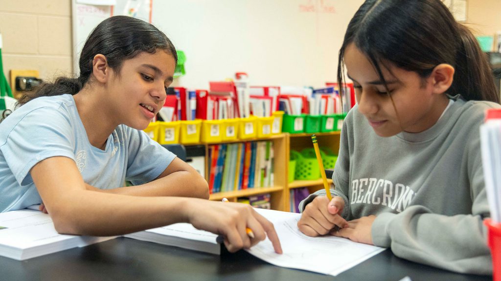 Children in a classroom help one another.