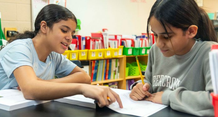 Children in a classroom help one another.