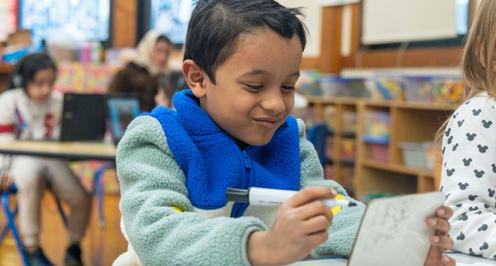 A young child writes on a small dry erase board and smiles.