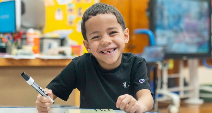 A young child writes on a small dry erase board and smiles.