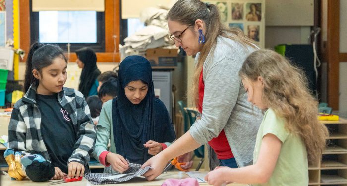 A teacher helps her students with cutting fabric.